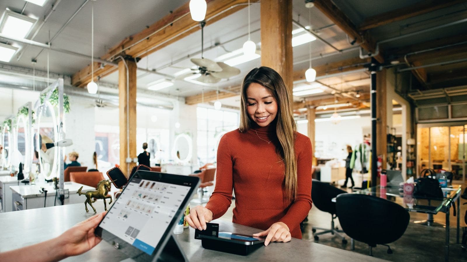 A small business owner serving a customer at the counter with a tablet — the point where a good website stops being decoration and starts doing work