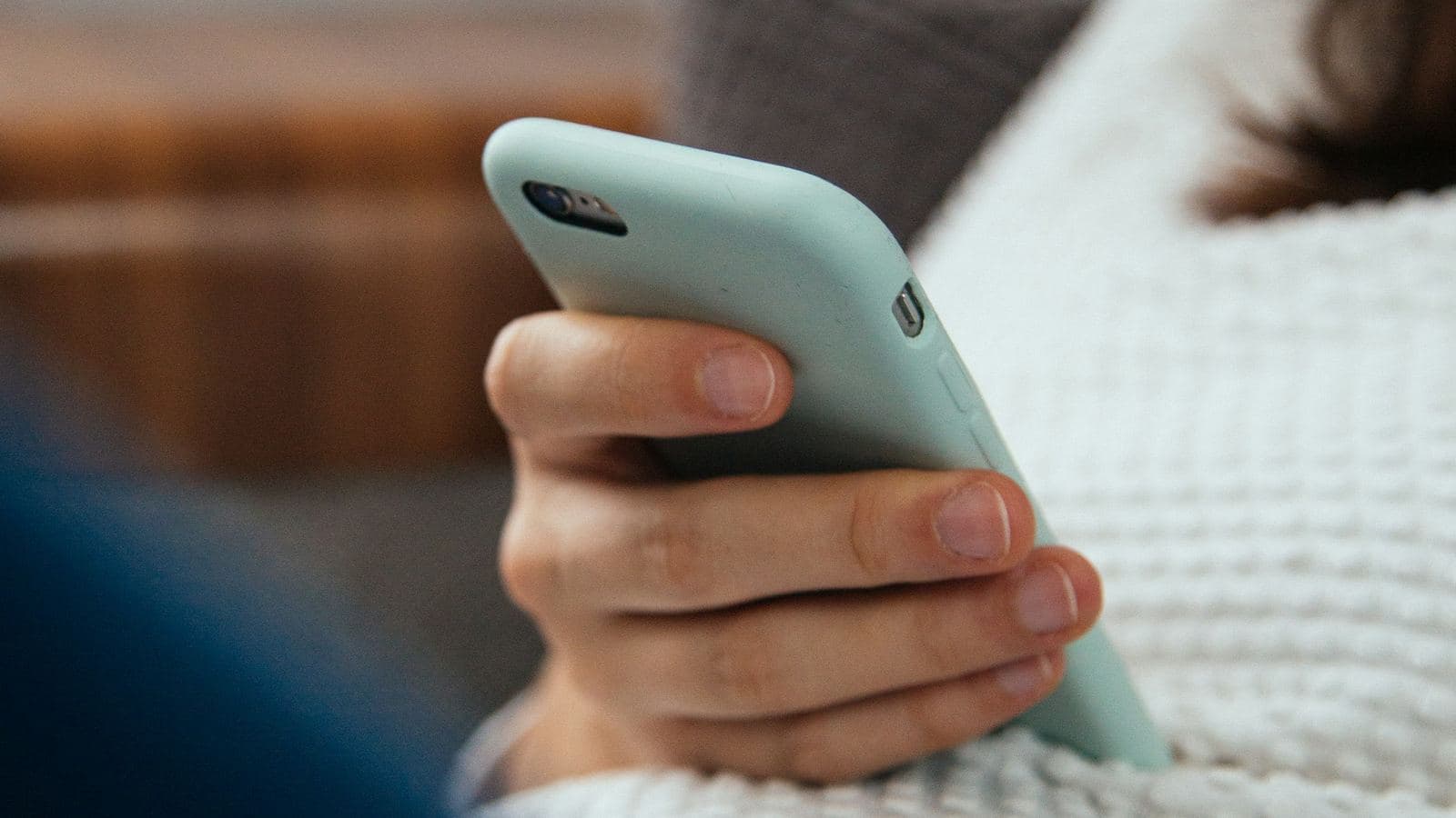 A person relaxing on a sofa in a cream knitted sweater, holding a mint-green smartphone in one hand. Most visitors now meet a business's website on a phone, where every saved round trip is easier to feel