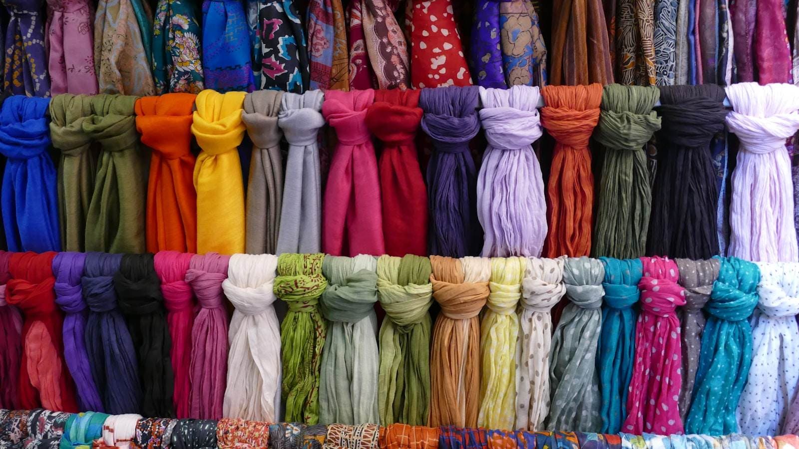 Rows of shawls and scarves stacked by colour — a real catalogue is variants, stock and specification, not just a photo grid