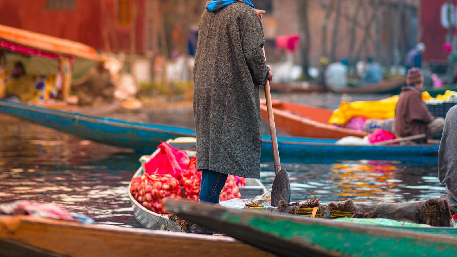 A vendor poling a shikara loaded with produce through Srinagar's floating market — commerce here has never lacked product, only distribution
