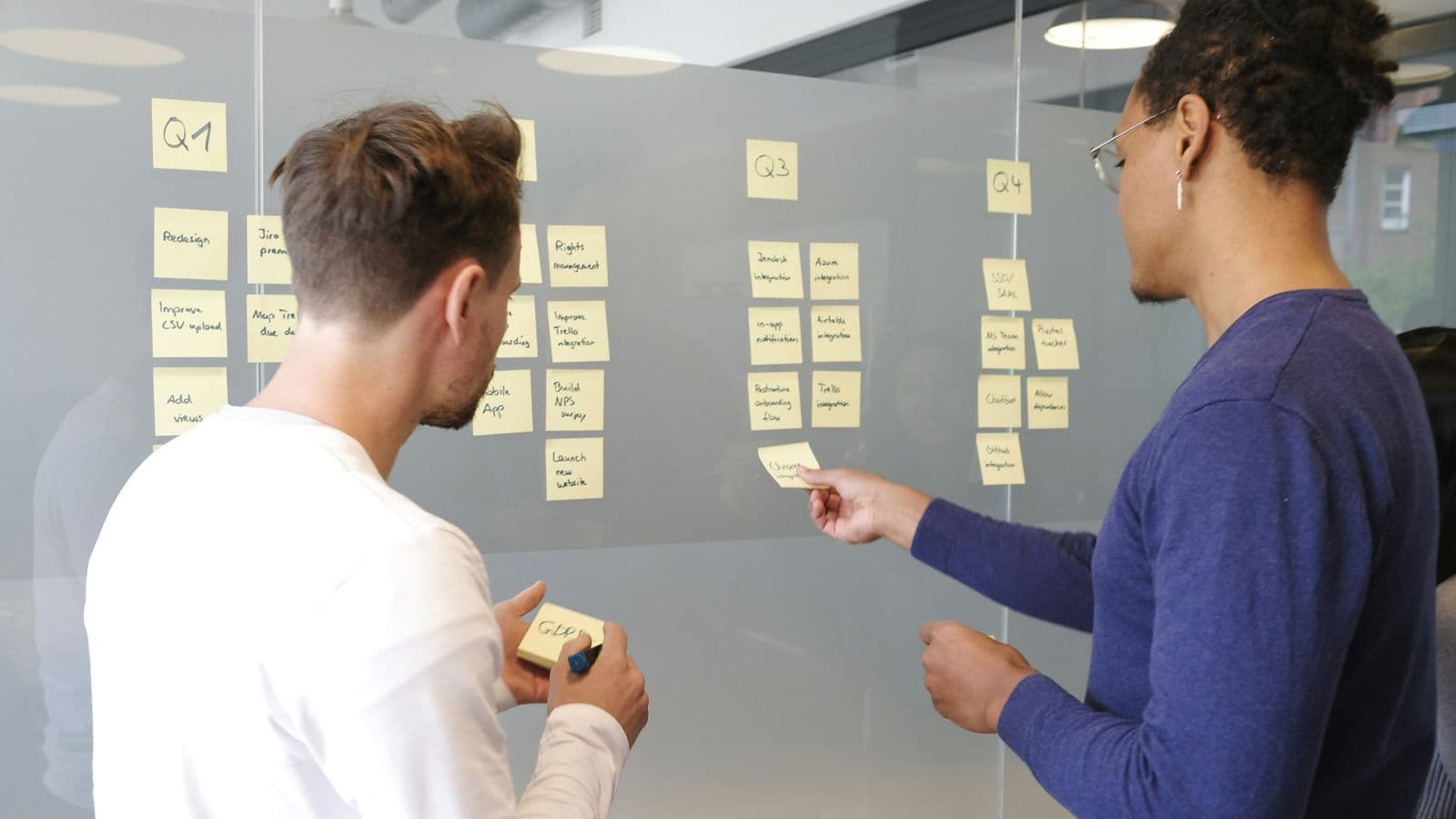 Two people mapping a flow on a glass wall with sticky notes — the fortnight of discovery that decides whether the next six months are productive
