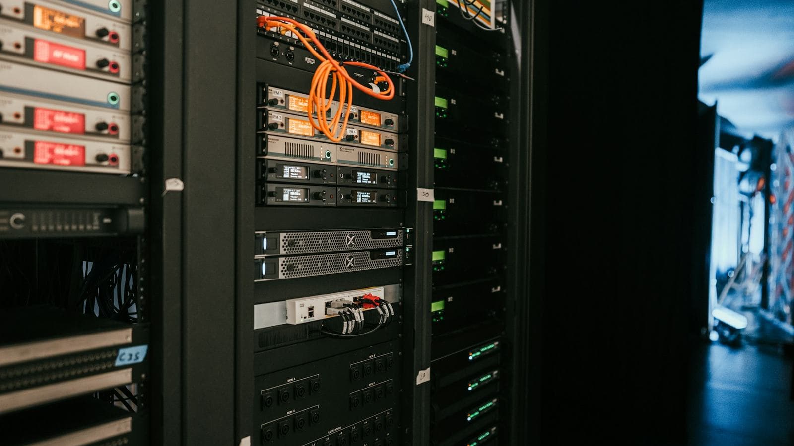 A row of server cabinets with orange patch cables and status displays glowing, a doorway open at the far end of the room. Whether you need this kind of setup depends far more on how the business depends on the site than on how many visitors it gets