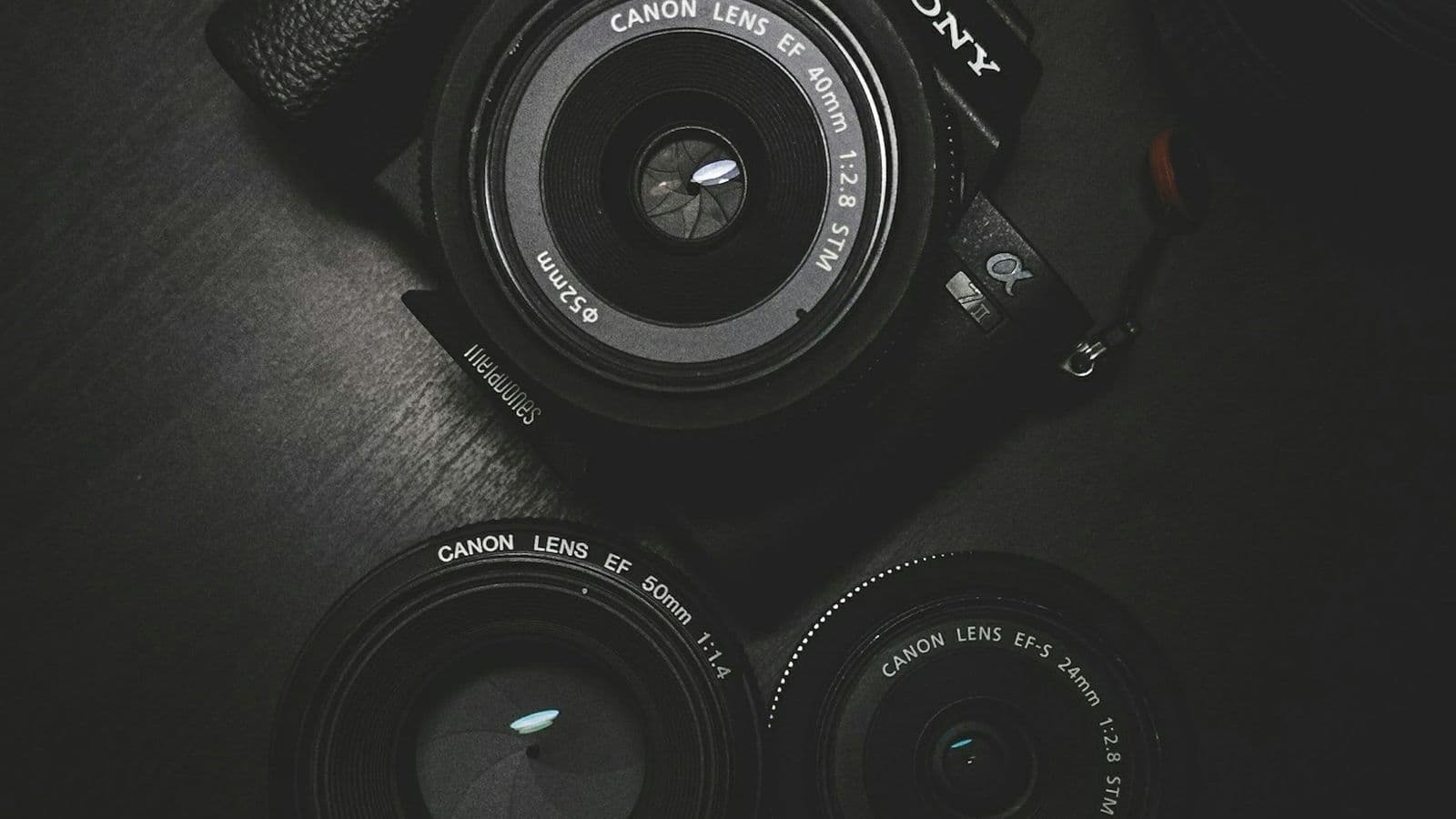 A Sony camera body and three Canon lenses arranged on a dark table. A single photo from a modern camera or phone can easily outweigh an entire well-built web page