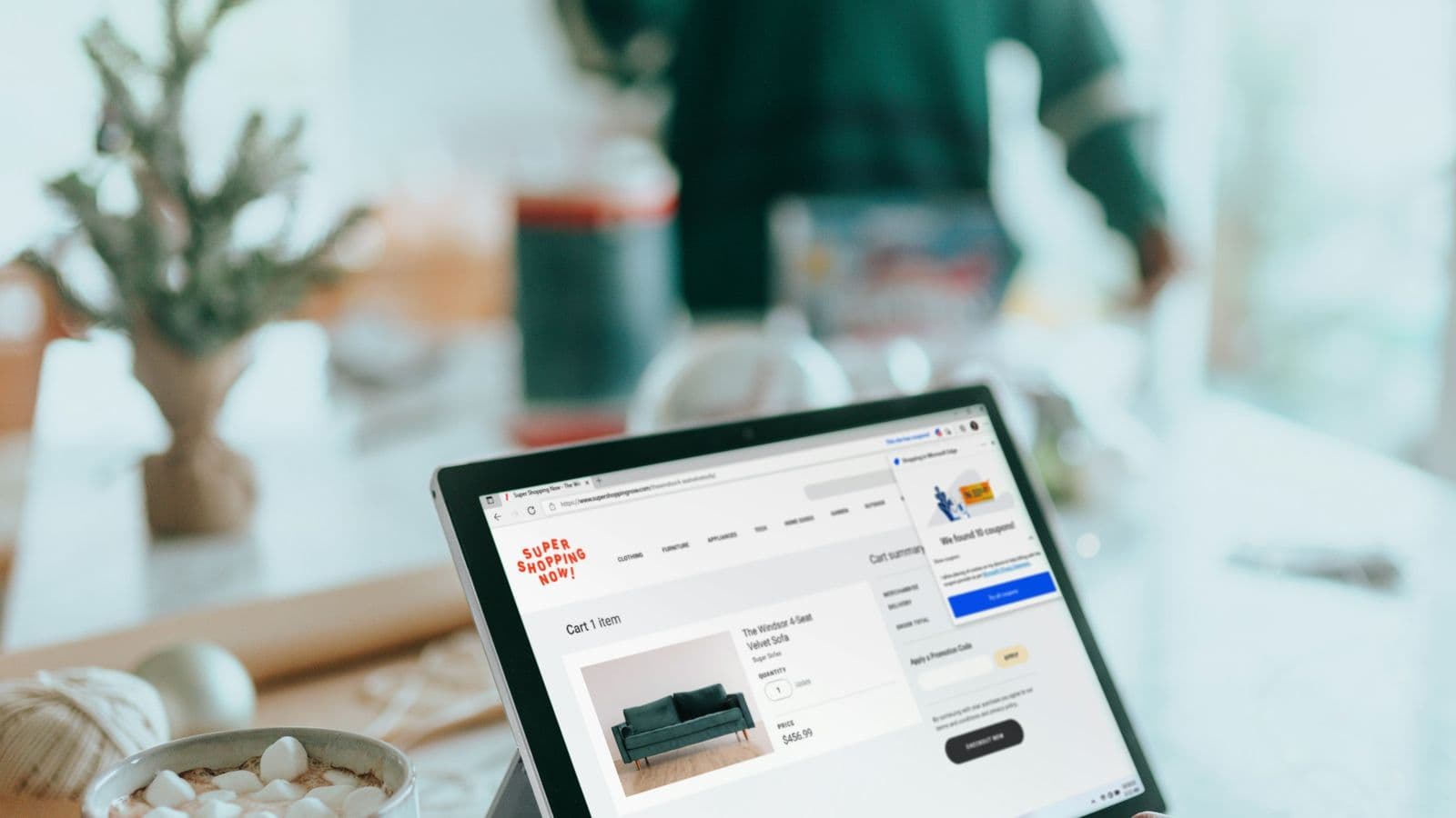 A laptop on a table showing an online store's shopping cart page with a sofa in the basket, next to a mug of hot chocolate. The checkout is where a slow page costs the most, because the visitor has already decided to buy
