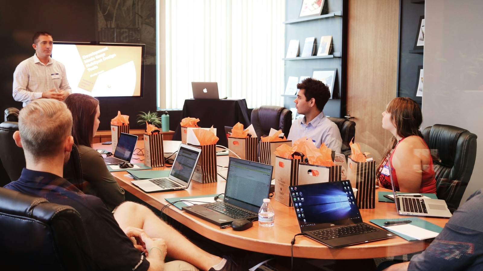 A team meeting around a long table with laptops open while one person presents at the front. Most intern projects end with a demo to the team