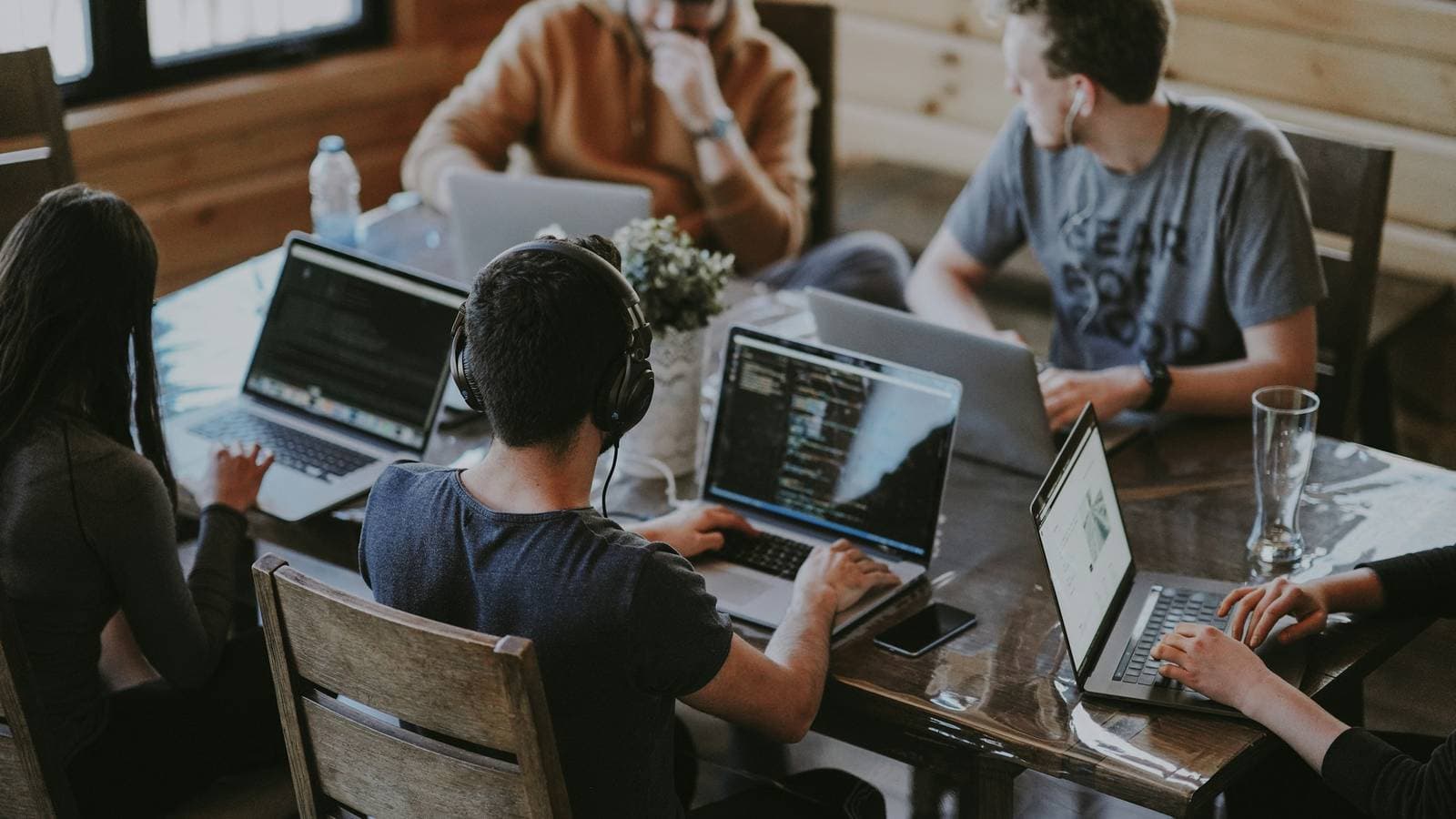 Four people working on laptops around a shared wooden table. Your first week in an internship is mostly setup, introductions and reading code you didn't write