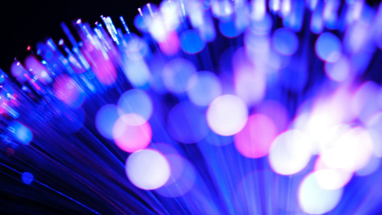 Blue and pink light glowing at the ends of fibre-optic strands. A message's trip from one phone to another crosses carrier networks, undersea cables and data centres in a fraction of a second