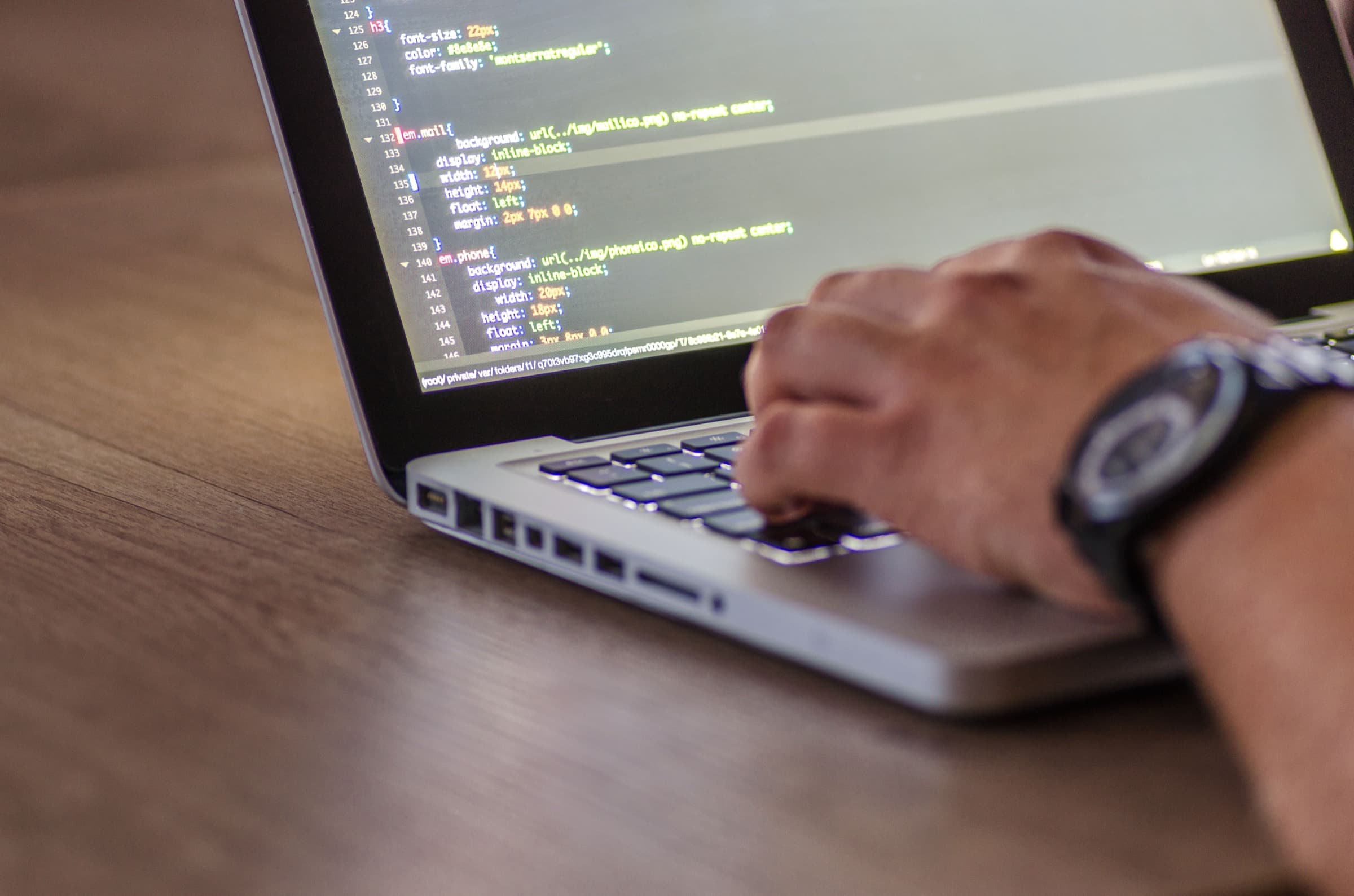 A developer's hand on a laptop keyboard with CSS open in the editor — delivery work running quietly behind an agency's brand