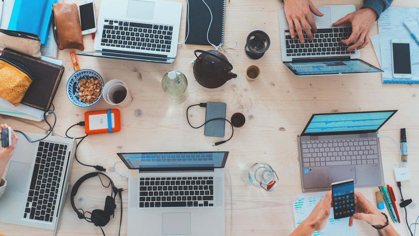 Several laptops and hands around one shared desk — the freelancer versus web development company decision, seen from above